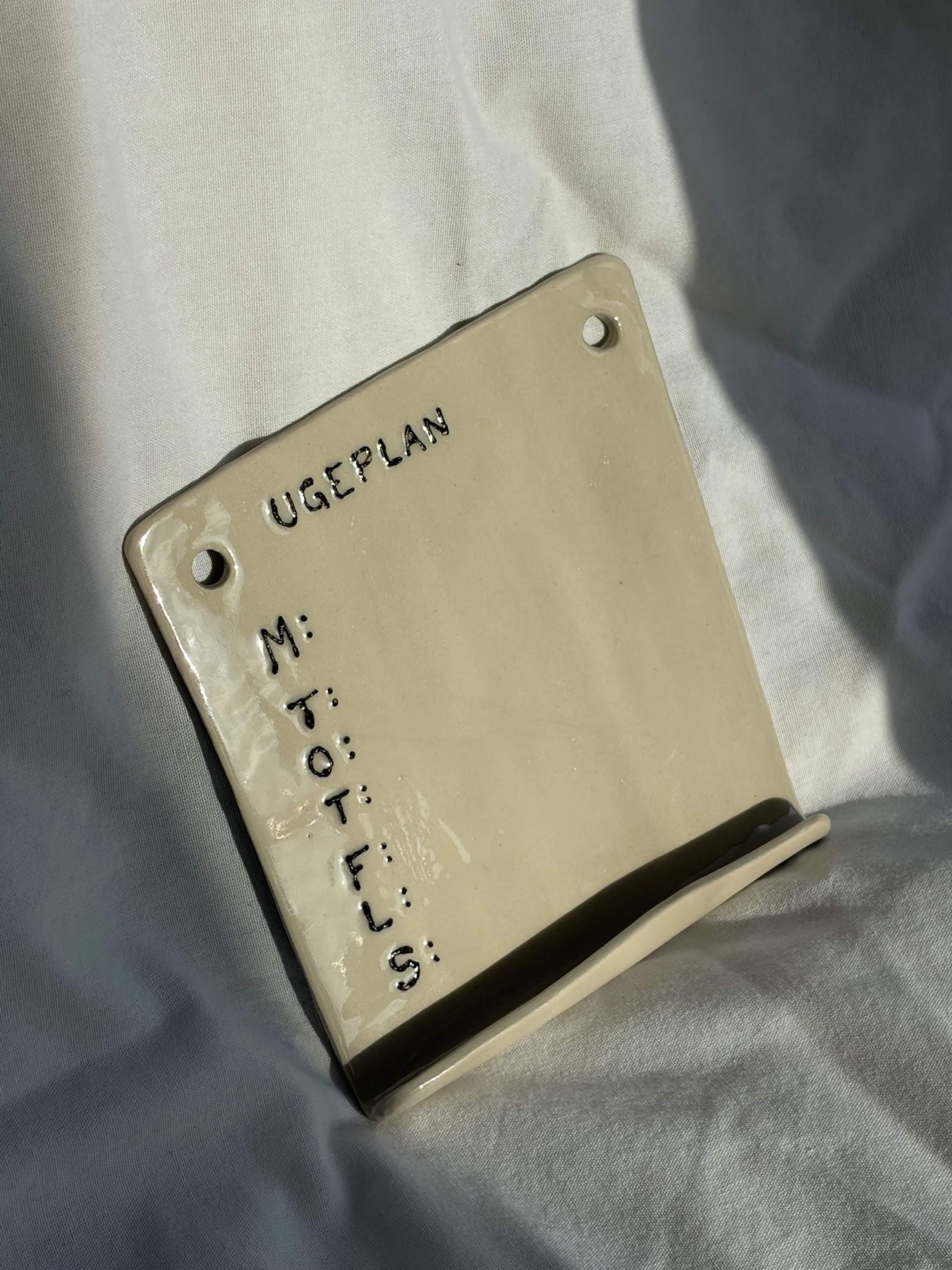 Håndformet keramisk ugeplan med indridset tekst på et lille stativ.